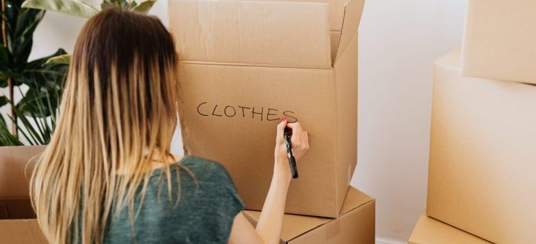 woman writing "clothes" on a cardboard moving box