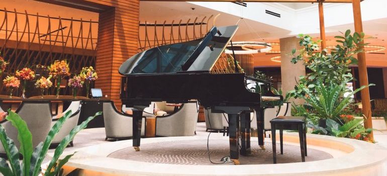 A piano in a well lit room waiting for piano moving