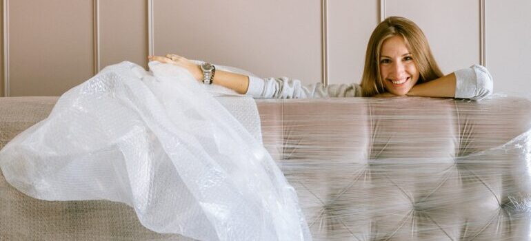 A woman unpacking a couch covered in wrapping.