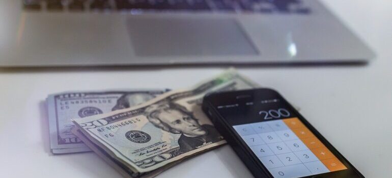 Dollar bills next to a phone and a laptop.