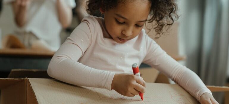 a little girl drawing on a box which is a great way to involve your kids in moving and packing process 