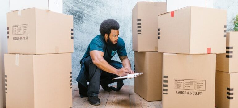 Professional movers will properly pack your belongings for safe transport, using supplies like boxes in the picture that a man i checking