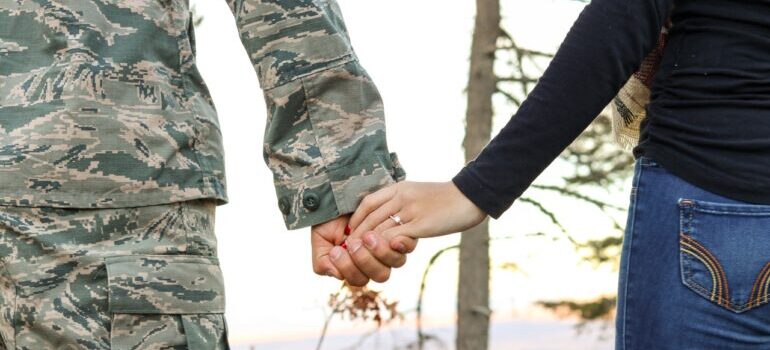 A solder and woman holding hands waiting for military movers