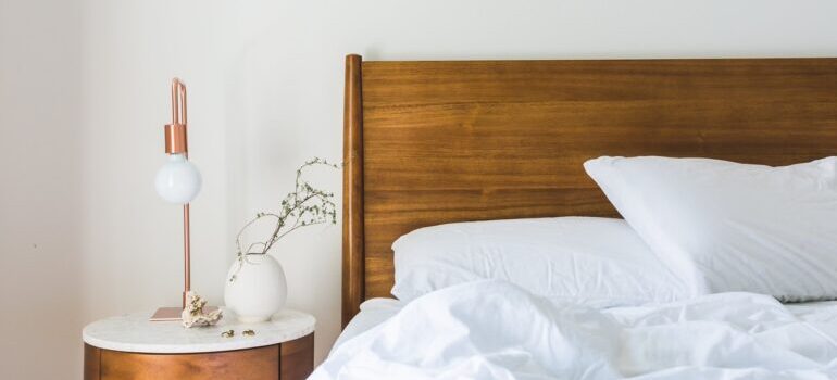 Bed, with the handstand next to it with a lamp and plant.