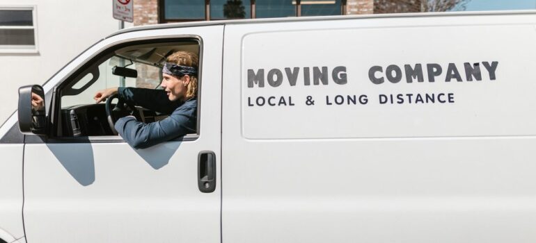 a man in the drivers seat of a white van that says "moving company"