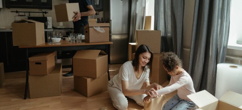 a mother packing items on the floor with her child while the father carries boxes in the background as a way to include your kids in your MD move