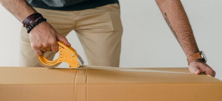 A person sealing moving box with a tape as if you hire residential movers when relocating across Canada they will do packing for you