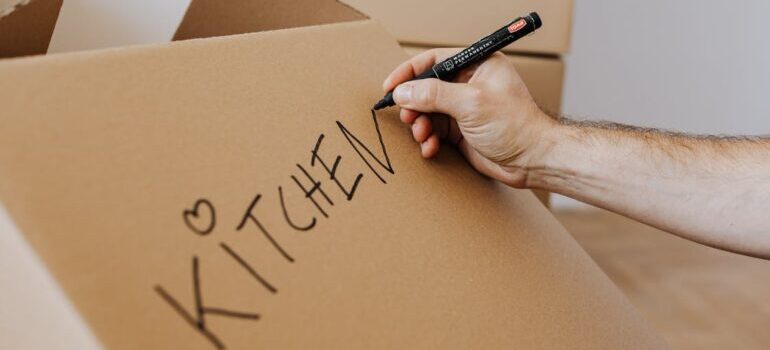 A person labeling a moving box writing kitchen 