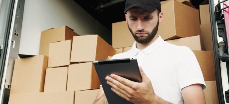 a man looking at his tablet while standing in front of a van full of cardboard boxes