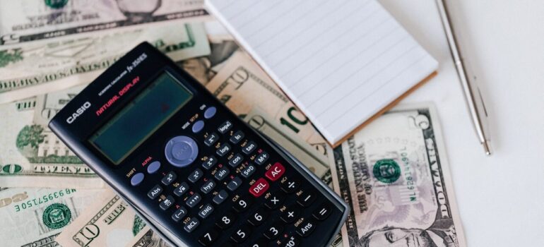 a pile of money with a calculator and a notebook on top of them to show that it is cheaper to move during the off-season