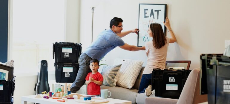 parent picking up a picture from the wall as they pack, while their child stands in the room with them