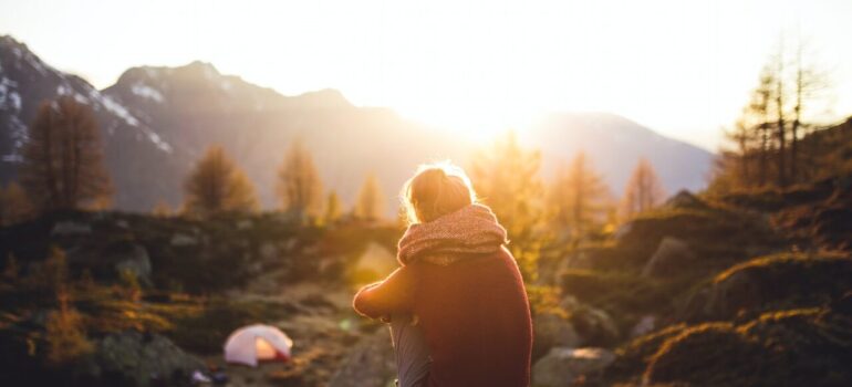 a person sitting on a rock while looking at the sun on behind the mountaints