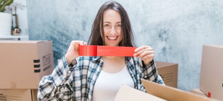 Woman surrounded by cardboard boxes holding packing tape 