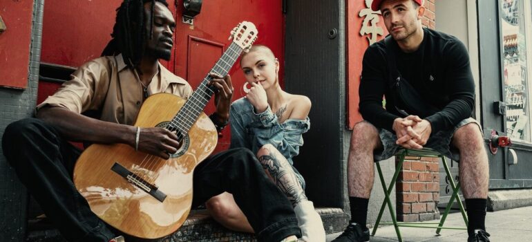 three young artists moving from VA to MD sitting on the street playing a guitar