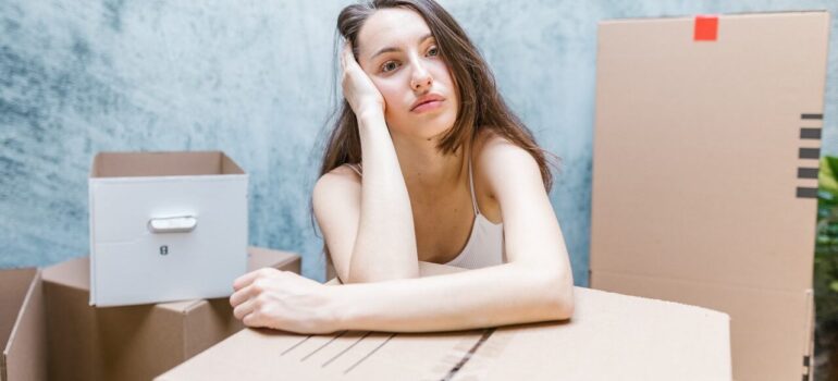 a woman leaning on a cardboard box thinking about hiring professional packers in DC area
