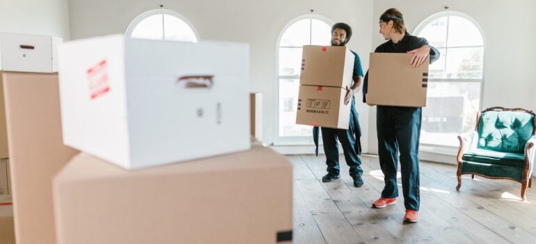 two moving crew personnel carrying cardboard boxes through a home
