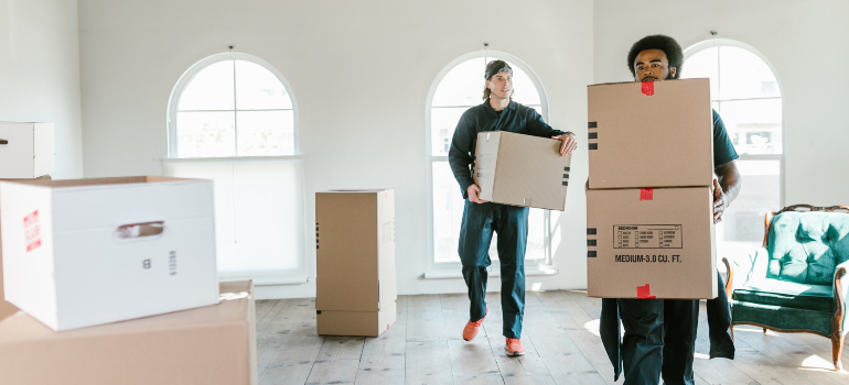 Moving professionals carrying heavy boxes inside a room.