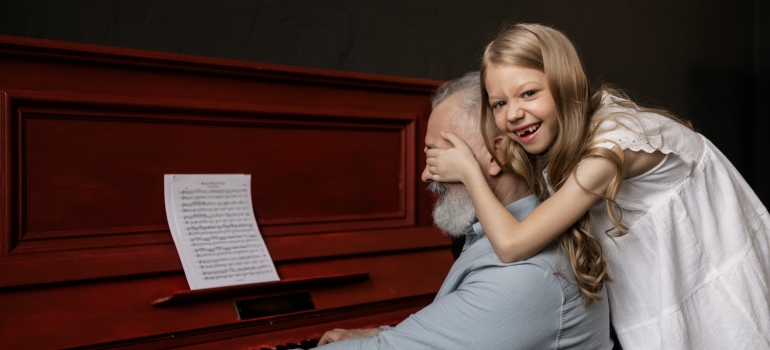 Picture of a girl and senior man playing in front of a piano 