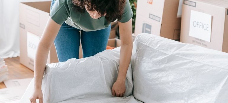 Woman wrapping a couch to prepare it for when movers hoist furniture when moving.