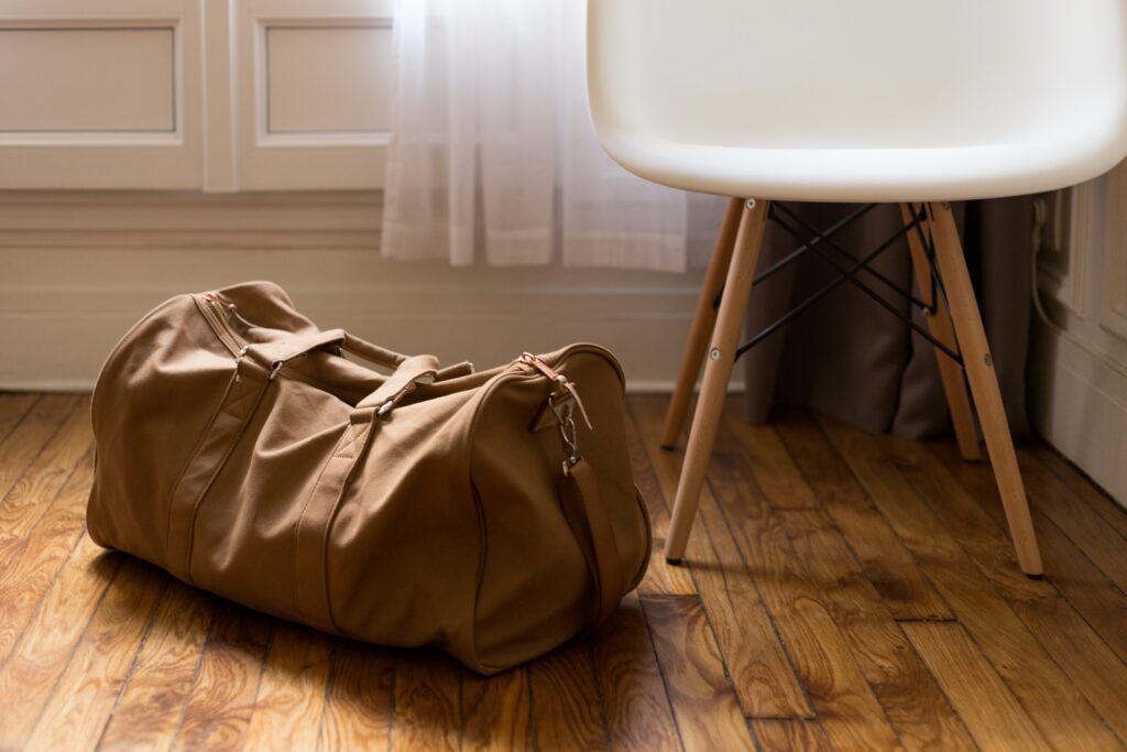 A brown duffle bag on the floor, next to a chair.