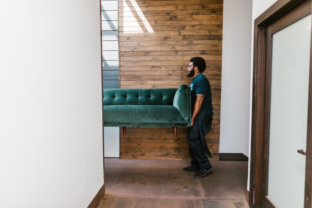 A professional mover carrying a green sofa.