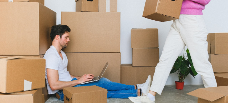 A man working on his laptop while sitting on the floor surrounded with a lot of boxes.