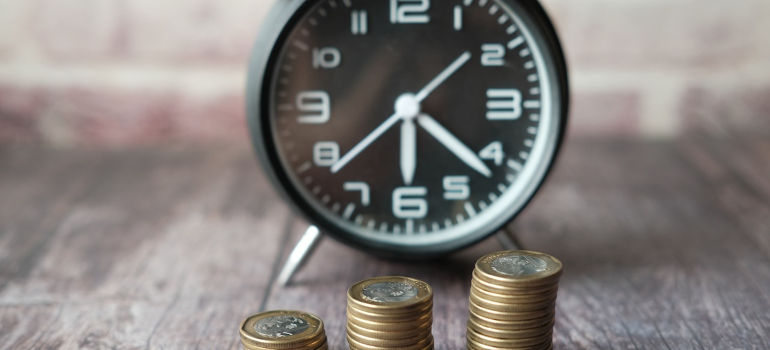 A black clock and three stacks of coins in front of it