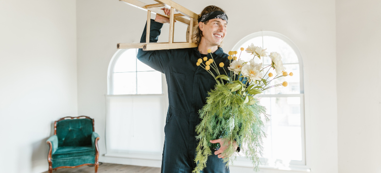 a man working for a moving company, carrying a plant and a stool