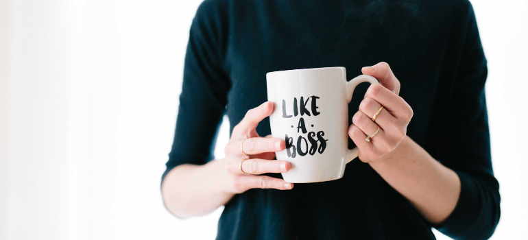  a woman in a black dress holding a mug that has "Like a boss" written on it