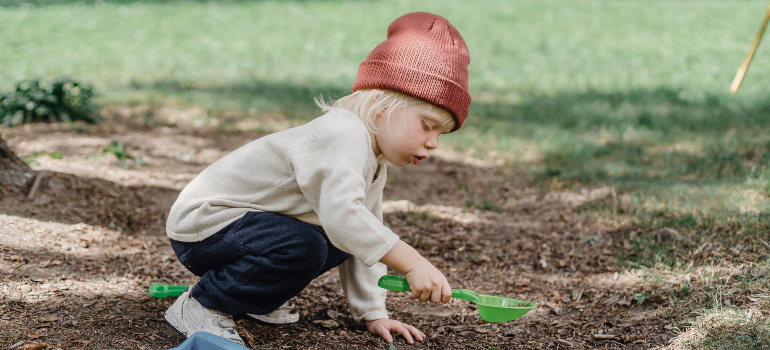 a little boy playing in his backyard while wearing a red hat