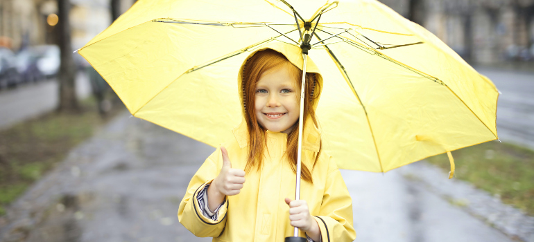 a little gear wearing a yellow raincoat while holding a yellow umbrella