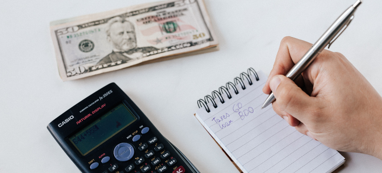 a person writing something on a notepad with a calculator and some money next to it