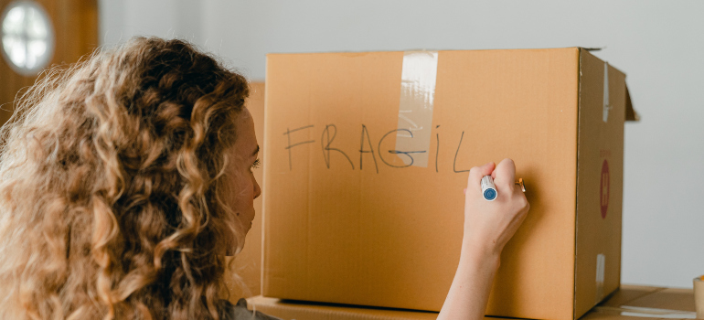 a woman writing the word "fragile" on a box which is a good way to pack before moving to Gaithersburg 