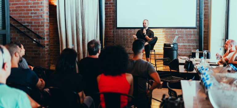 a person speaking at a conference while sitting in a chair on the podium