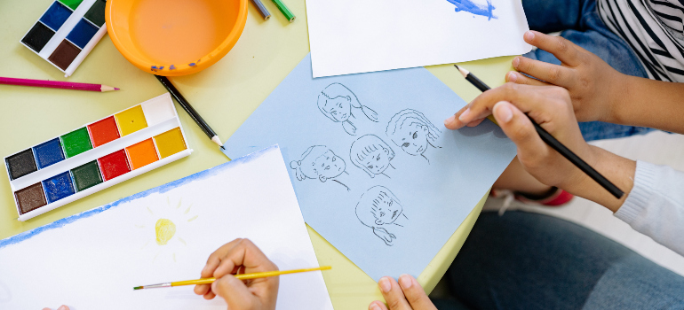 a child's and adult's hands above papers where they draw 