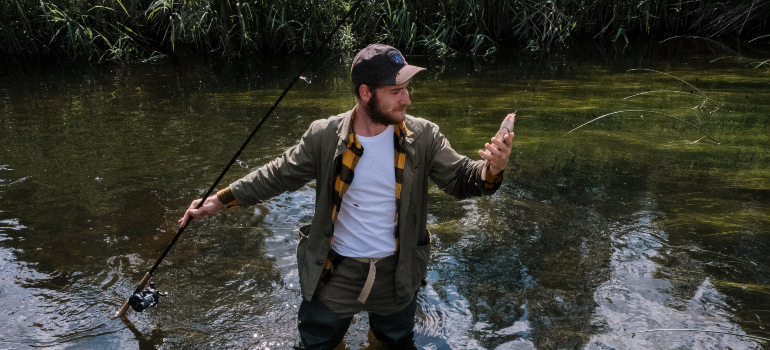 a man catching a fish while standing in shallow water at one of the top fishing spots in the DMV area