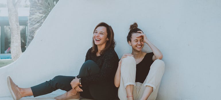 two women sitting next to a wall and laughing together