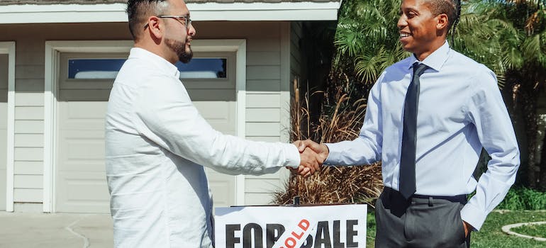 two people shaking hands in front of a house that has just been sold