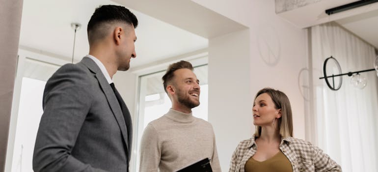 two people talking to a real estate agent very excitedly while thinking about what not to say when buying a new home