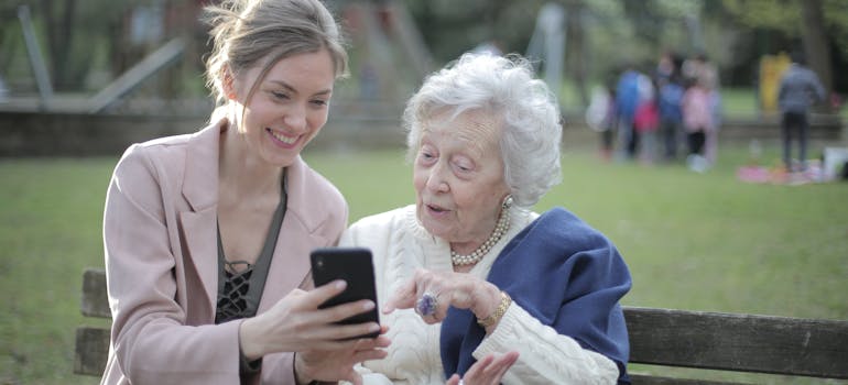 a woman showing her elderly mother a communication app on her phone which you should do if you want to help your elderly parents move to Bethesda MD