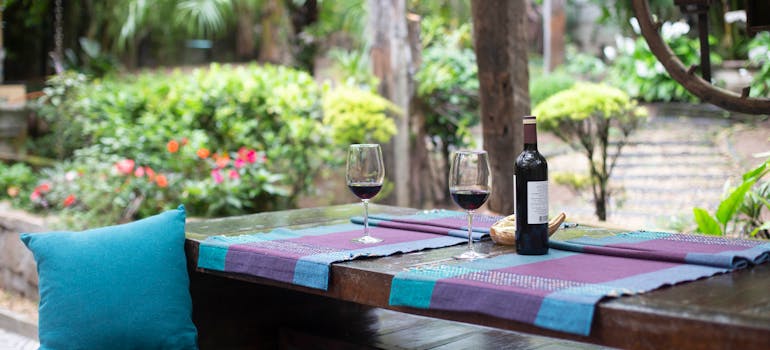 a table in the backyard with two glasses and a bottle of wine on it