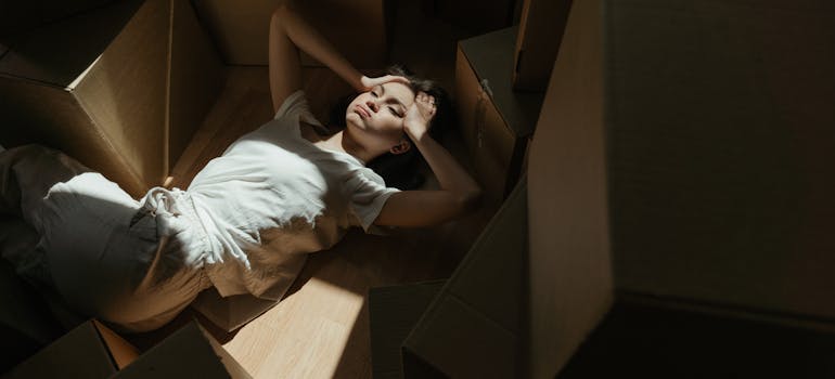 a woman lying on top of some boxes and wondering which one to use to pack for the move in a Tetris way