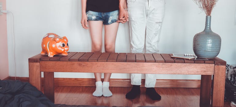 two people holding hands and standing next to a table with a piggy bank on top of it