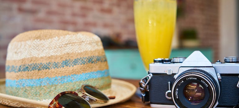 a hat, glasses, a cup of juice, and a camera on the table