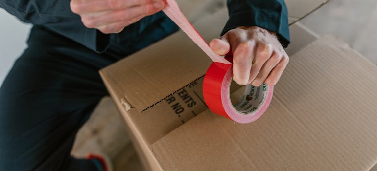 a man sealing a cardboard box with a red duct tape