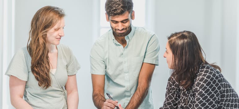 two happy people signing a paper in front of a woman in a black and white shirt