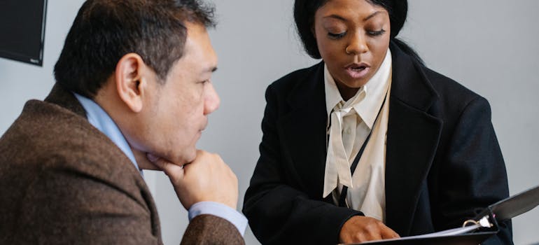 a woman helping a man with some paperwork, which is one of the biggest benefits of hiring a real estate agent