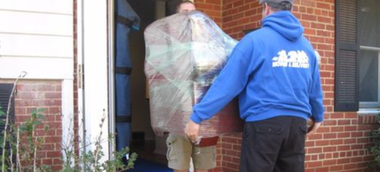 two men carrying a wrapped piece of furniture