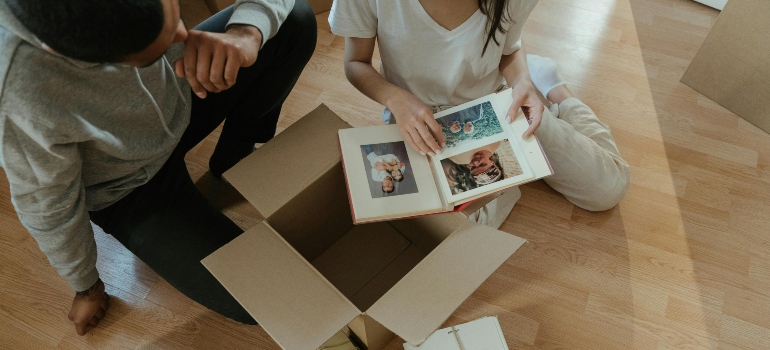 A couple are sitting on the floor and looking at a photo album.