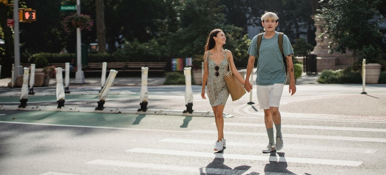 A happy couple is holding hands and walking across the street.